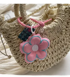 Close-up of pink fabric flower pendant with blue knit trim on straw bag handle