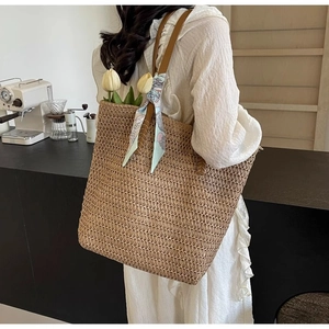 Large woven straw tote bag with brown handles and a blue printed silk scarf for summer
