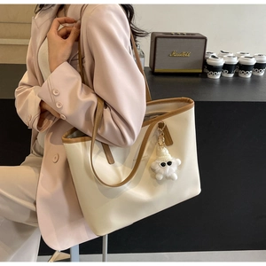 Close-up of cream tote bag with brown trim and cute plush monster charm accessory
