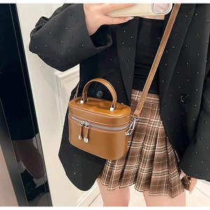 Sac seau cylindrique en cuir marron porté avec un blazer pour un look élégant