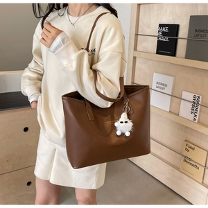 Close-up of brown leather tote bag with gold logo and plush monster charm detail