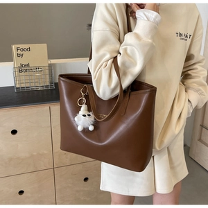 Detailed view of brown tote bag with plush charm and gold branding on premium faux leather