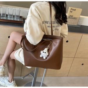 Brown leather tote bag featuring a cute white plush pendant shown in a lifestyle street setting
