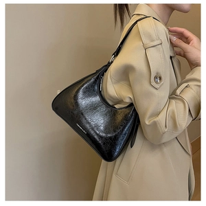 Close-up of black hobo bag with cracked leather texture on beige trench coat