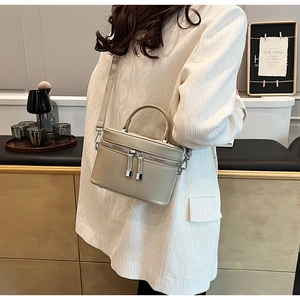 Détail d'un sac seau en cuir beige avec double fermeture éclair porté en bandoulière