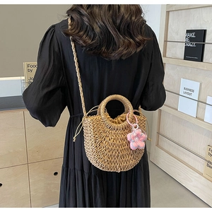 Detail of hand-woven straw crossbody bag with pink floral charm and drawstring lining
