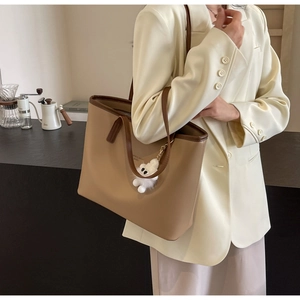 Close-up of beige leather tote bag with brown straps and cute bear charm detail