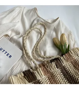 Detail of multi-color woven straw tote with fringe trim and braided rope straps on white fabric