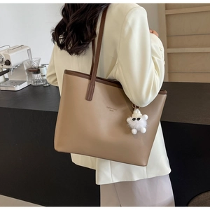 Close-up of a khaki leather tote bag with a white plush monster charm on the side