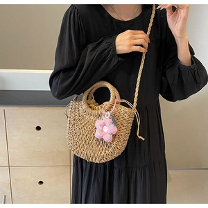 Detail of hand-woven straw bag with pink flower charm and drawstring closure