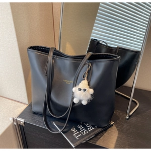 Detail of black PU leather tote bag featuring gold branding and a cute plush charm