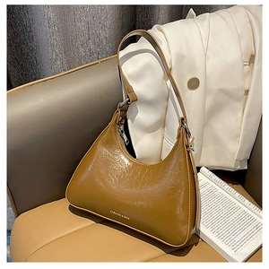 Detail of a brown leather hobo bag with a glossy finish on a cream-colored sofa
