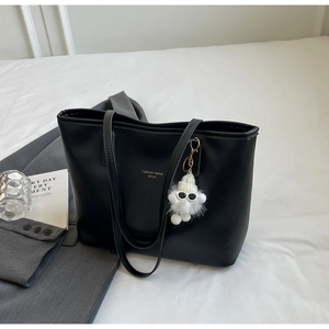 Close-up of black PU leather tote bag with gold lettering and plush monster charm