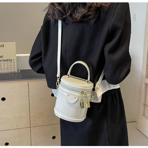Detail view of white quilted cylinder bag with gold lock charms and smooth leather texture