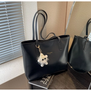 Detail of black tote bag featuring gold lettering and a cute plush character charm