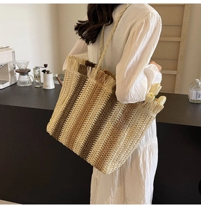 Detail of hand-woven straw tote bag with striped pattern and fringe edge in lifestyle setting