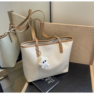 Detail of white tote bag with brown trim, featuring a cute plush monster charm and lettering