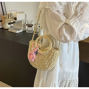 Detail of woven straw bag featuring a beige drawstring liner and pink flower charm