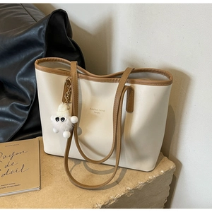 Detail of cream leather tote bag with brown straps and a cute plush bear charm