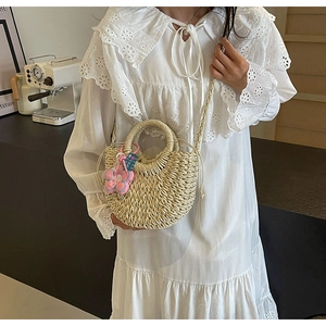 Detail of hand-woven beige straw bag with pink floral charm and ring handle