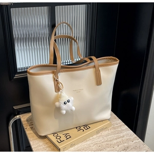 Detail of a minimalist cream tote bag with brown trim and a plush monster charm