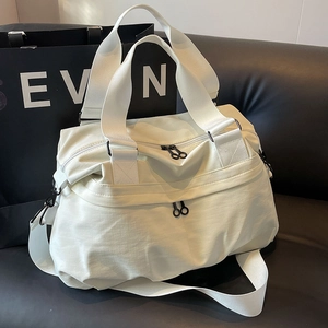 Large cream nylon tote bag with black straps and hardware on a black leather sofa