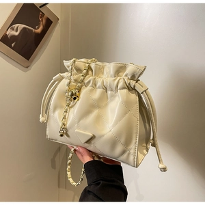 Close-up of quilted cream bucket bag with gold chain strap and metal triangle logo