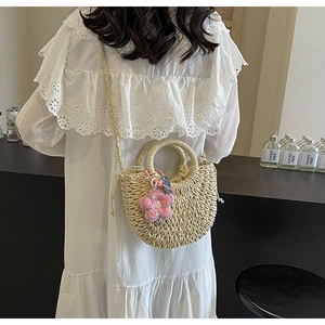 Detail of woven straw crossbody bag with pink flower charm and round handle