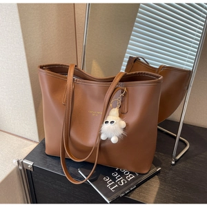 Detailed view of brown leather tote bag with white plush charm in a lifestyle interior setting