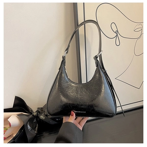 Close-up of black glossy PU leather underarm bag with pleated texture and silver buckle