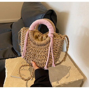 Detail of woven straw bag with pink rope handles and tassel accents for beach vacation