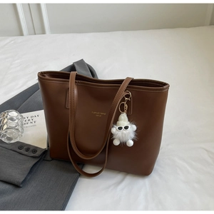 Detailed view of a brown leather tote bag with a cute white plush doll charm