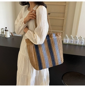 Detailed close-up of woven straw tote bag with blue stripes and decorative fringe edges