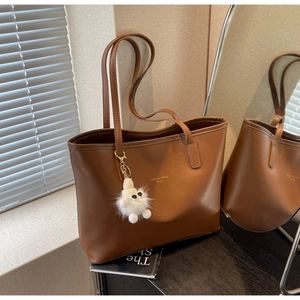 Detail of deep brown leather tote bag with gold lettering and plush white charm