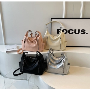 Détail de quatre sacs hobo texturés en rose, blanc, noir et argent sur un piédestal