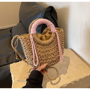 Detail of woven straw handbag featuring pink tasseled handles and a drawstring liner