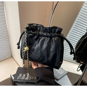 Macro shot of black quilted bucket bag with chain strap and triangle plaque