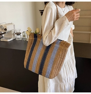 Detail of blue and beige striped straw tote bag featuring frayed tassel edges and tulips