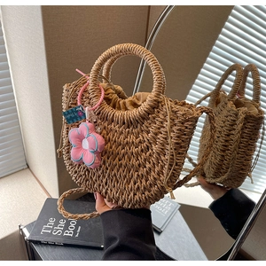 Detail of woven straw handbag with a circular handle and a pink flower charm accessory