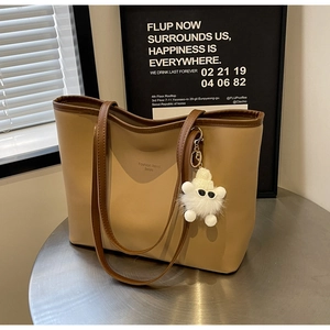 Detail of light brown tote bag with Senjio branding and a cute white plush monster charm