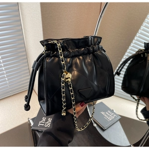 Detail of black quilted bucket bag with gold chain strap and skull charm detail