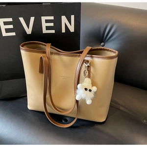 Detail of khaki tote bag with plush cartoon charm on a luxury black leather sofa