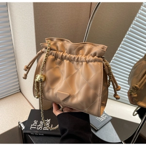 Macro detail of beige quilted bucket bag with gold chain strap and drawstring closure