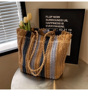 Detail of woven straw tote bag with navy stripes, fringe trim and woven handles