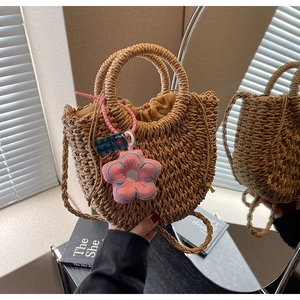 Detailed close-up of handmade woven straw bag with pink flower charm and drawstring liner