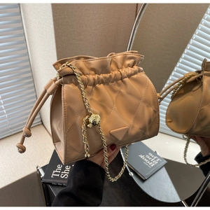 Close-up of quilted beige bucket bag with chain strap and triangular leather patch