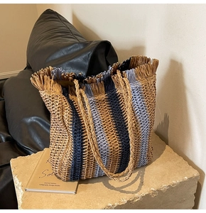 Detail of woven straw tote bag with navy stripes and fringed edges on stone base
