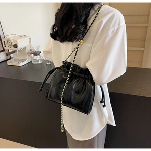 Detail of black quilted bucket bag with chain strap and gold adjustment ball