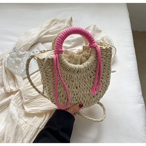 Detail of woven straw handbag featuring a pink wrapped handle and fringe tassel accents