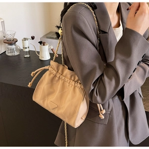 Close-up of beige quilted chain bag with drawstring closure and metal triangle logo detail